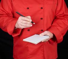 chef de uniforme vermelho segurando um caderno em branco e um lápis de madeira preto foto