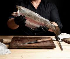 chef em uma camisa preta e luvas de látex pretas segura uma carcaça crua de peixe salmão sem cabeça foto