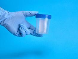 mão em luvas estéreis de látex segurando um frasco de plástico vazio para exames médicos foto