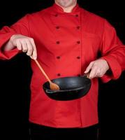 cozinhe de uniforme vermelho segurando uma frigideira preta vazia e uma colher de pau foto