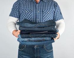 homem de jeans e camisa xadrez azul segurando uma pilha de jeans foto