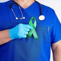 médico de uniforme azul e luvas de látex segura uma fita verde como símbolo de pesquisa inicial e controle de doenças foto