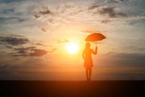 silhueta de uma mulher segurando um guarda-chuva na praia e no pôr do sol foto