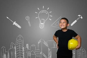 menino usando um chapéu amarelo de engenheiro e idéias de planos de casa no quadro-negro foto