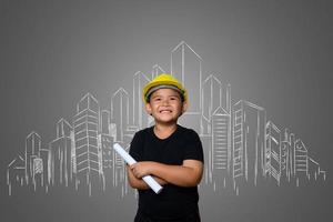 menino usando um chapéu amarelo de engenheiro e idéias de planos de casa no quadro-negro foto