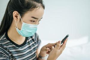 garota usando uma máscara higiênica, camisa listrada e segurando um telefone celular foto