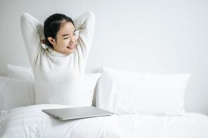 jovem se espreguiçando na cama com um laptop foto