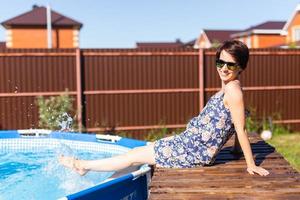 retrato de uma bela jovem de pijama sentada perto da piscina inflável - verão e conceito de vida no campo foto