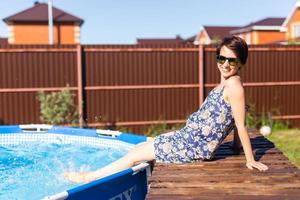 retrato de uma bela jovem de pijama sentada perto da piscina inflável - verão e conceito de vida no campo foto