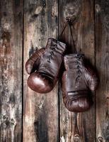 luvas de boxe marrons de couro muito velhas penduradas em uma velha parede de madeira surrada foto