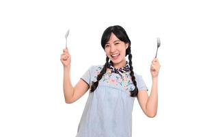 retrato da bela jovem mulher asiática sorrir em vestido jeans com colher e garfo no fundo branco foto