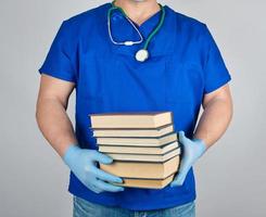 médico de uniforme azul e luvas de látex estéreis segura uma pilha de livros na mão foto
