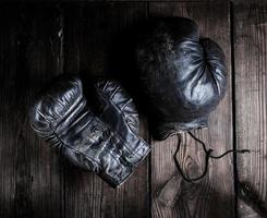 luvas de boxe pretas muito velhas em um fundo de madeira marrom foto