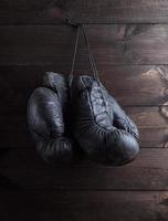 par de luvas de boxe de couro preto surradas muito velhas penduradas em um prego foto