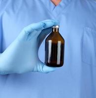 médico de uniforme azul e luvas de látex segurando um frasco de vidro marrom com remédio para tratamento foto
