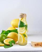 bebida refrescante de verão limonada com limões, folhas de hortelã, limão em uma garrafa de vidro foto