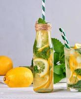 bebida refrescante de verão limonada com limões, folhas de hortelã, limão em uma garrafa de vidro foto