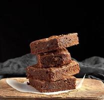 pilha de pedaços quadrados assados de bolo de brownie de chocolate na tábua de madeira marrom foto