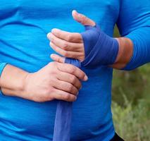 atleta fica de pé e envolve as mãos em bandagem elástica têxtil azul foto