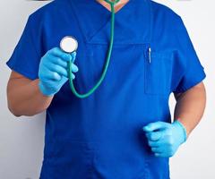 médico de uniforme azul e luvas estéreis segurando um estetoscópio médico foto