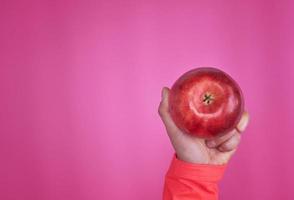 maçã vermelha madura em uma mão feminina em um fundo rosa foto