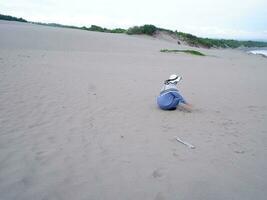 costas da mulher de chapéu que estava sentada e jogando areia da praia, a vista da areia foto