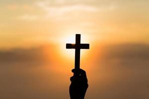 silhueta de mãos de mulher rezando com cruz no fundo do nascer do sol da natureza, crucifixo, símbolo de fé. oração de crise da vida cristã a deus. foto