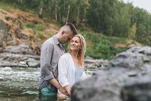 casal jovem feliz apaixonado por viajantes se beijando no rio da montanha foto