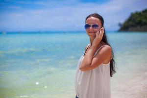 jovem mulher bonita na praia falando em seu telefone foto