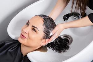 cabeleireiro profissional lavando cabelo de jovem no salão de beleza foto