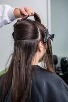 cabeleireiro aplica uma máscara de cabelo em cabelos pretos lisos. cuidados com os cabelos no salão de beleza. foto