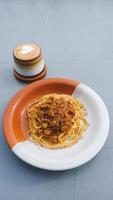 prato saudável de espaguete italiano coberto com um saboroso tomate e molho à bolonhesa de carne moída e manjericão fresco em uma mesa cinza. servido com capuccino foto