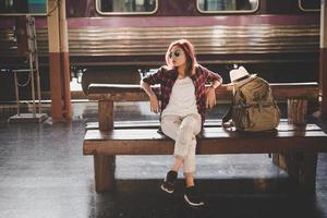 jovem hippie turista com mochila sentada na estação de trem foto