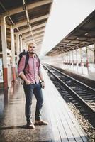 jovem hippie esperando na plataforma da estação com mochila foto