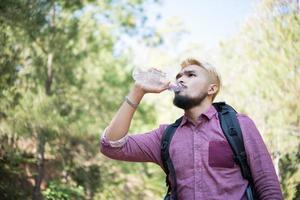 feliz hipster homem turista com mochila caminhando na floresta foto