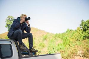 jovem fotógrafo sentado em sua caminhonete fotografando uma montanha foto