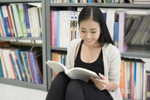 jovem estudante asiática na biblioteca lendo um livro