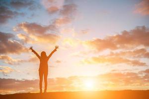 feliz silhueta jovem de uma mulher pulando contra o belo pôr do sol foto