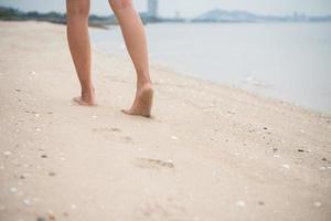 jovem caminhando na praia de areia deixando pegadas na areia foto