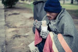 morador de rua enrolado em um pano comendo macarrão