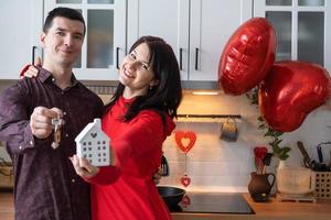 homem e mulher apaixonados namoram em casa na cozinha com as chaves da casa. dia dos namorados, casal feliz, história de amor. ninho de amor, hipoteca, realocação, compra, imóveis, moradia para família jovem foto