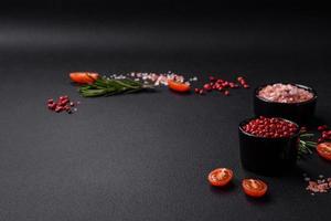 ingredientes sal, especiarias, ervas e tomates em um fundo escuro de concreto foto