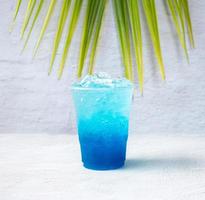 bebida havaiana azul em um copo de plástico e folhas de coco. foto