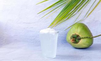 bebida de água de coco gelada em um copo de plástico e coco no fundo branco foto