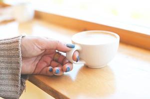 caramelo de café - café de mulher com a mão segurando uma xícara na mesa de madeira, xícara de café de caramelo no café da manhã - macchiato de caramelo quente no inverno foto