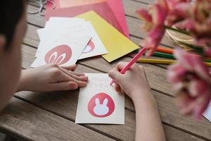 menino fazendo cartão de páscoa. materiais para criatividade artística na mesa infantil, pintura infantil. atividade de artesanato em papel no jardim de infância ou aprendendo em casa foto