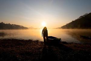 mulheres rebocando um barco para a costa no reservatório durante o nascer do sol, parque florestal harirak huai nam man reservatório loei tailândia 21 de janeiro de 2023 foto