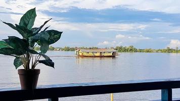 navio bandong ou kapal bandong no rio kapuas, oeste de kalimantan. vista da beira do rio kapuas com uma planta no vaso. céu azul claro. foto