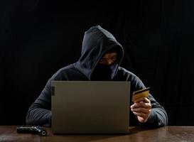 hacker espião homem uma pessoa com capuz preto sentado em uma mesa olhando computador laptop usado segurança de ataque de senha de login para circular dados digitais no sistema de rede da internet, fundo escuro noturno. foto