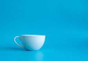 fotografia de vista superior da xícara de café branco em um pires branco, o interior do copo parece vazio. esperando que o café quente seja reabastecido para beber para se sentir revigorado e alerta sobre um fundo azul. foto